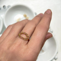 A light and airy open oval gold ring; lacy with organic holes; shown with scattered tiny rubies of various sizes; shown on hand