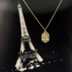 Textured, lacy, lemon-shaped pendant, shown in 14k yellow with diamonds; set against a black and white photo of the eiffel tower