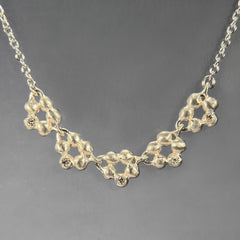 silver necklace with bottom component featuring 5 links that are open clusters of buds; each cluster has 1 diamond