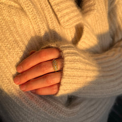 An oblong shape-ring made of ultra-lacy, modern filigree, with 5 diamonds running horizontally from one end to the other; shown worn on a hand; ultra fuzzy cream colored sweater in background