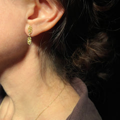 textured earrings with negative space made up of two similar components: there are two imperfect rectangles that hang end to end, each with an emerald; shown in 14k yellow; shown on ear, face in profile