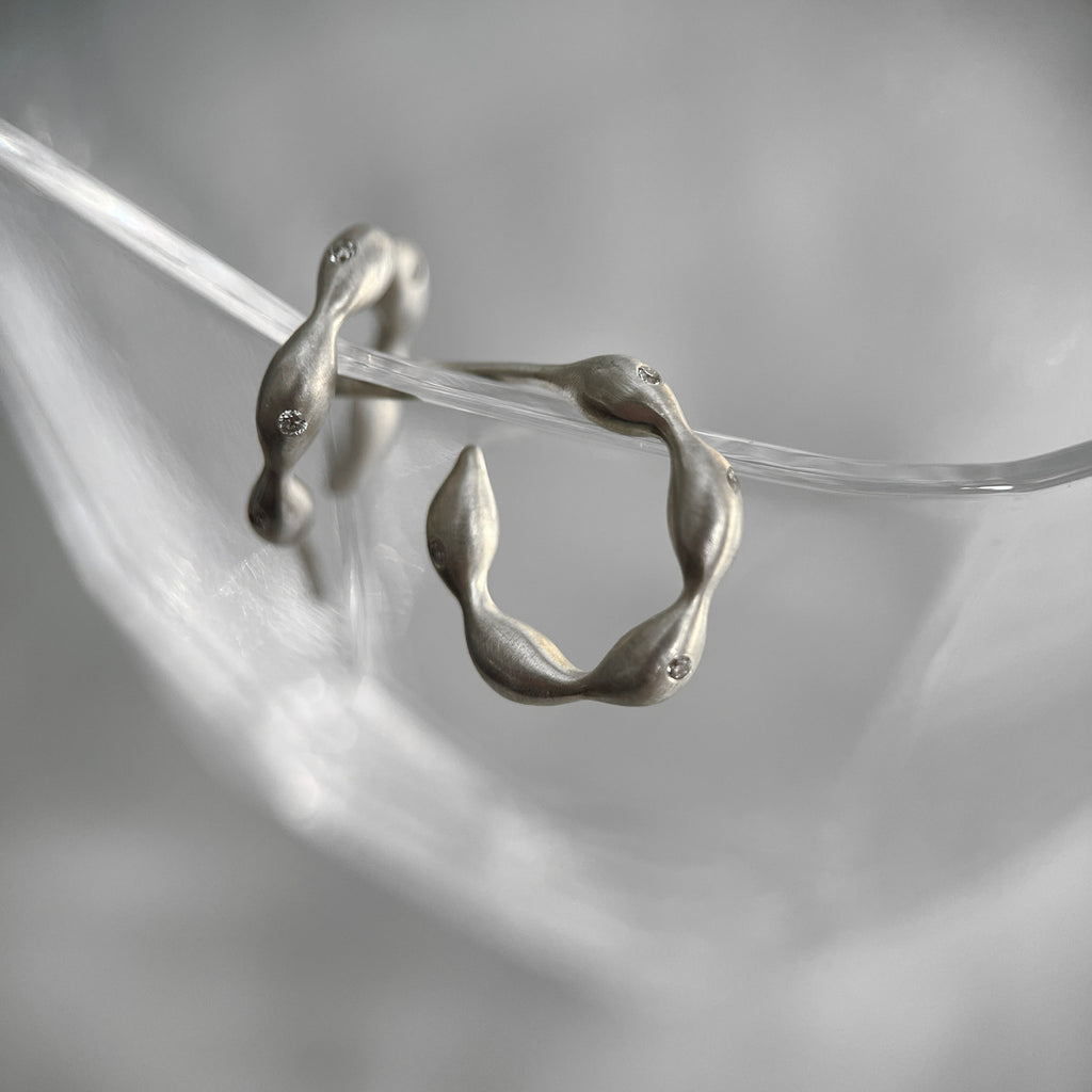 a pair of hoop earrings with undulating ribbons of seaweed or elongated seaweed bulbs; there are tiny scattered diamonds