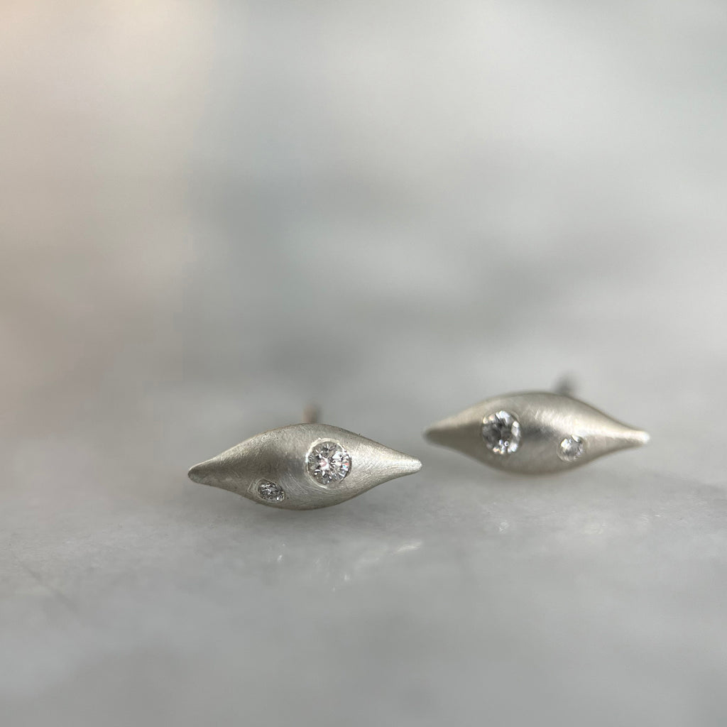 a pair of pod-like 3D studs with a satin finish and two diamonds in each rests on a marble counter