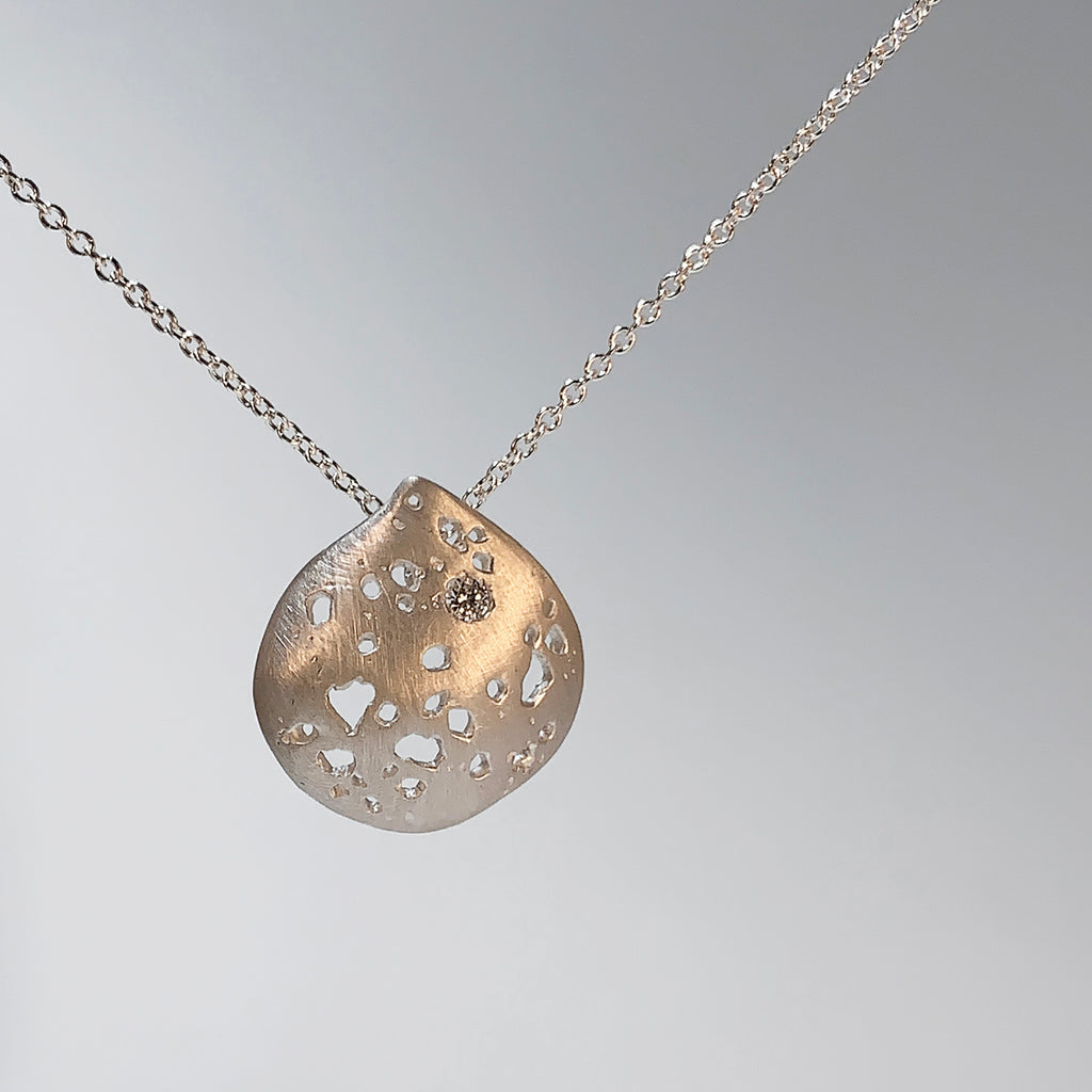 A soft, rounded shape that comes to a short point at the top; has random jagged cutouts throught, and a diamond in one of these spaces; a chain runs through a hidden bail on the back