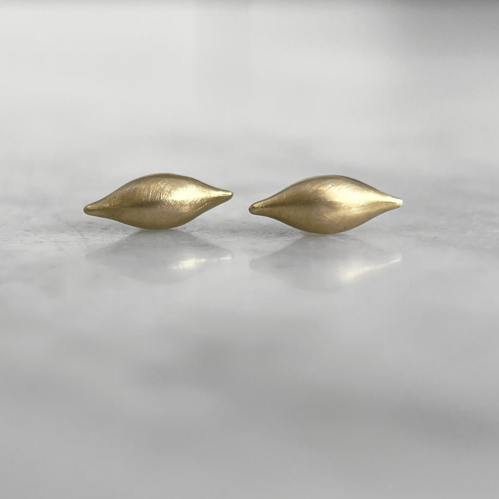 a pair of pod-like 3D studs in yellow gold with a satin finish rests on a marble counter