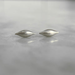 a pair of silver pod-like 3D studs with a satin finish rests on a marble counter