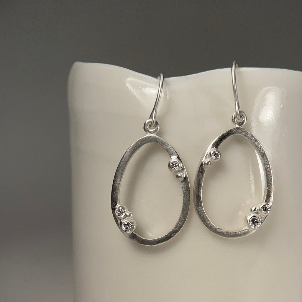 Thin, outlined, egg-shaped, wire earring in silver, with 3 diamond "buds" placed asymmetrically