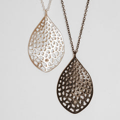 symmetrical, stylized leaf shaped pendant, filled with tiny, irregular cutouts and punctuated by a single diamond in the bottom quarter of the piece; shown in matte and blackened silver