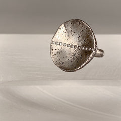 Large, round concave disk in slightly blackened silver, one with a stripe of diamonds up and down; angled view