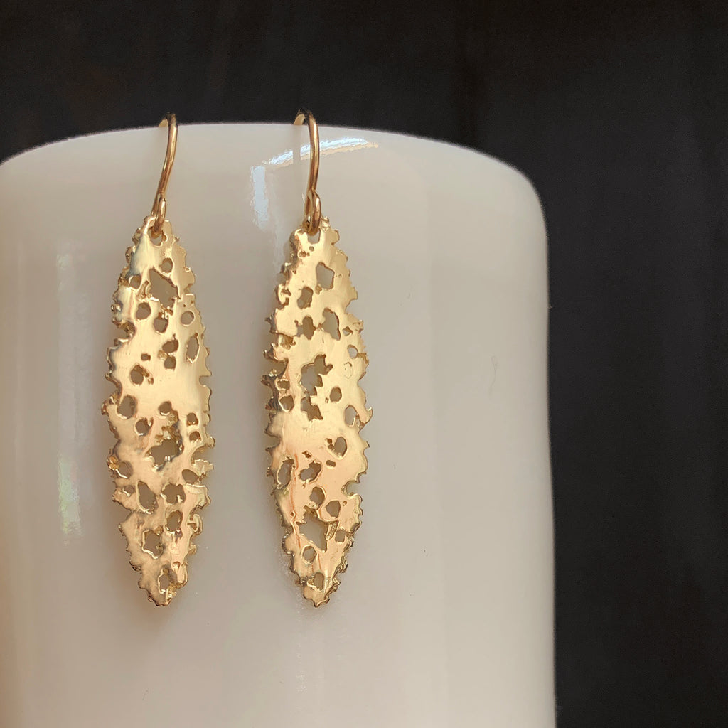 Shiny ellipse-shaped earring on wire, with organic holes, shown in yellow gold.