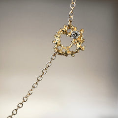 Tiny, lacy, textured element on chain, with elements of negative space and a white diamond set off-center